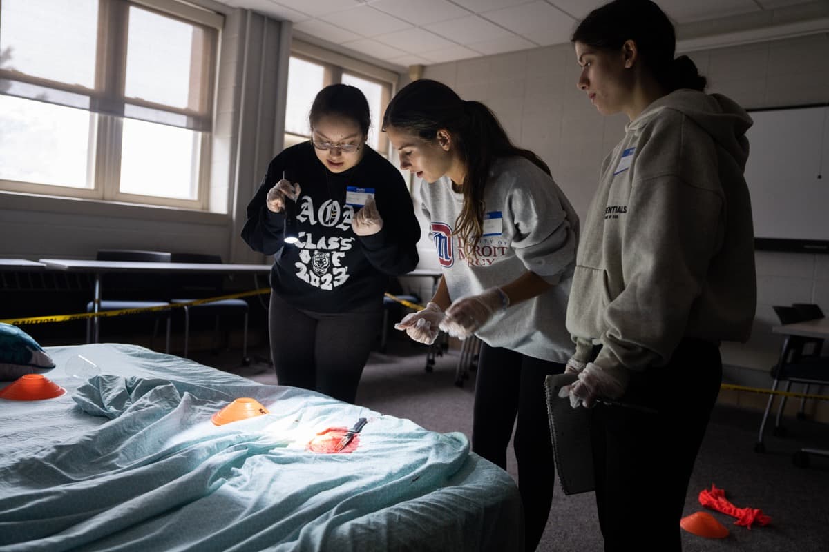 Three students investigating a crime scene using a flashlight