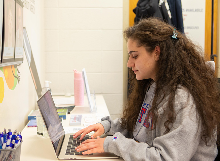 A student sits at a table and uses her computer.