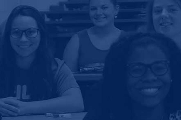 Two female students sitting in a classroom with other students smiling